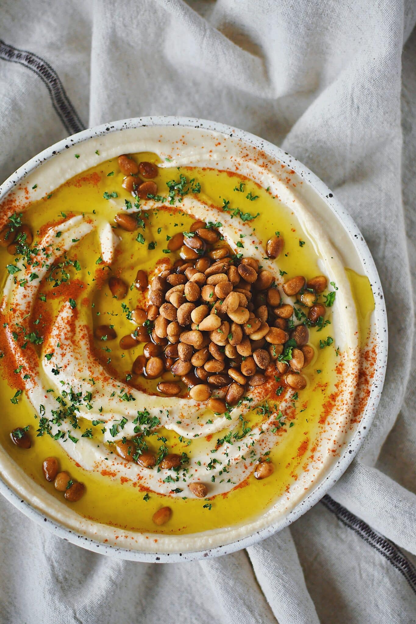 Homemade Hummus, topped with olive oil, paprika, toasted pine nuts, and parsley, ready to eat.