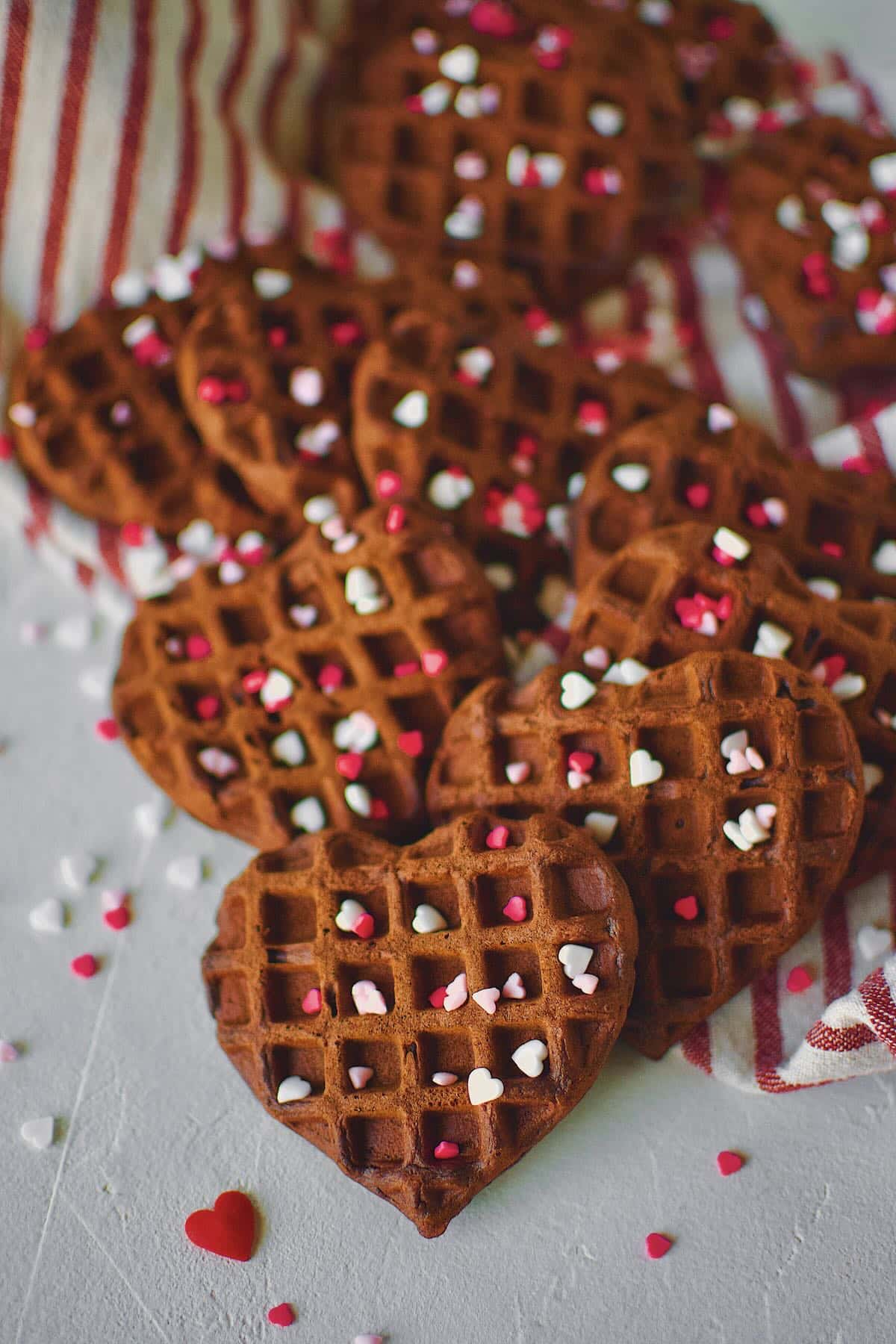 Red Velvet Waffles in the shape of hearts on a tray topped heart sprinkles.