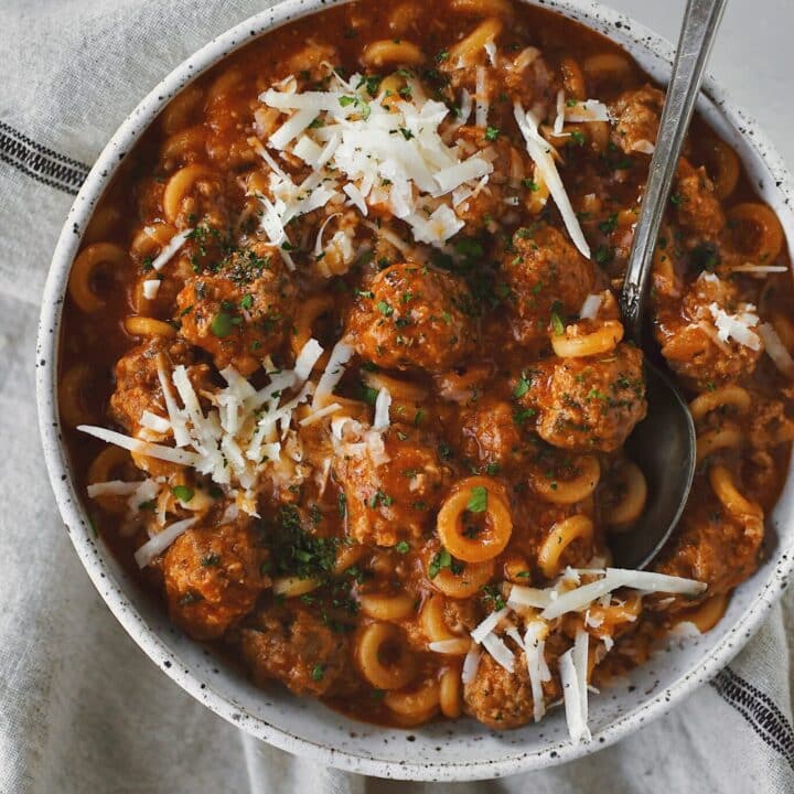 Homemade Spaghettios with meatballs in a bowl with a spoon topped with extra cheese and parsley.