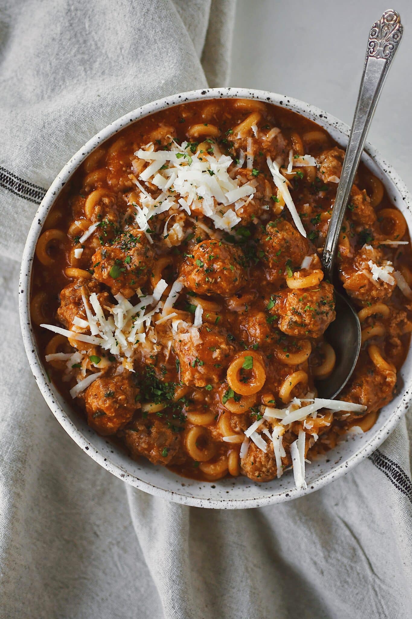 Homemade Spaghettios with meatballs in a bowl with a spoon topped with extra cheese and parsley.