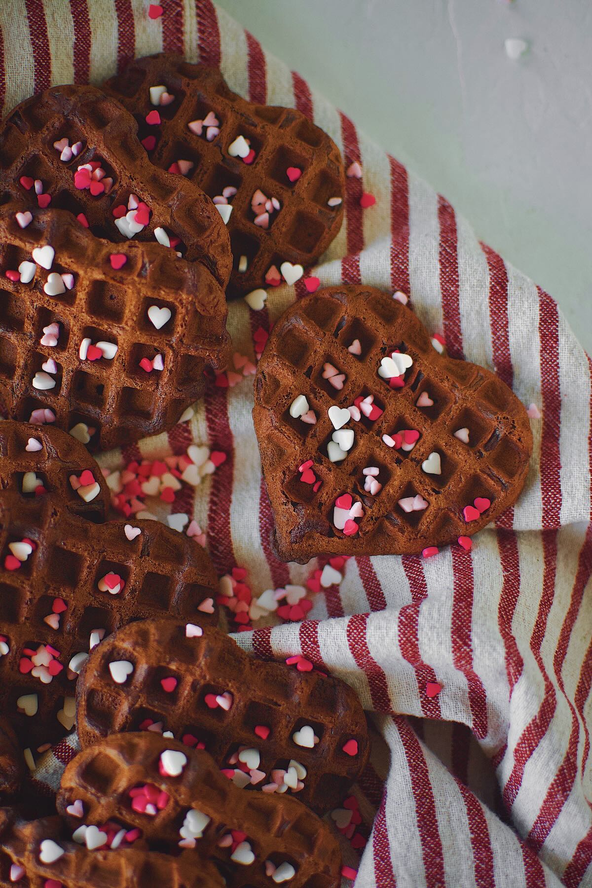 Red Velvet Waffles in the shape of hearts on a tray topped heart sprinkles.