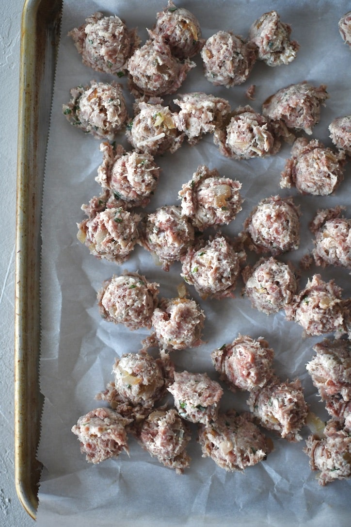Portioned out meatball mixture into tiny meatballs, on a tray.