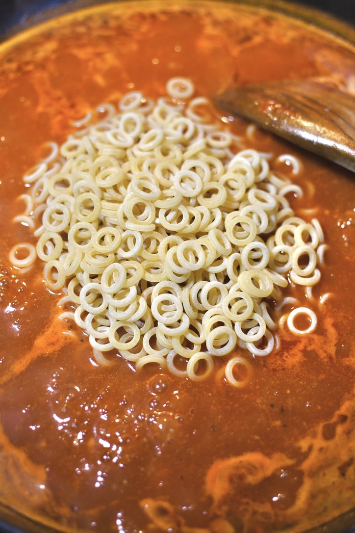 Placing the pasta in the pan with the sauce.