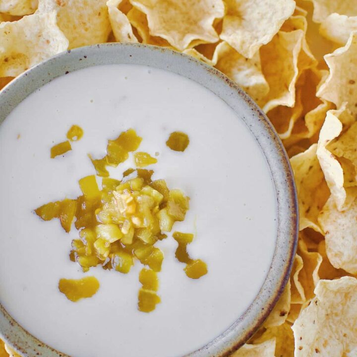 White Queso Dip in a bowl, surrounded by chips, topped with green chilis.