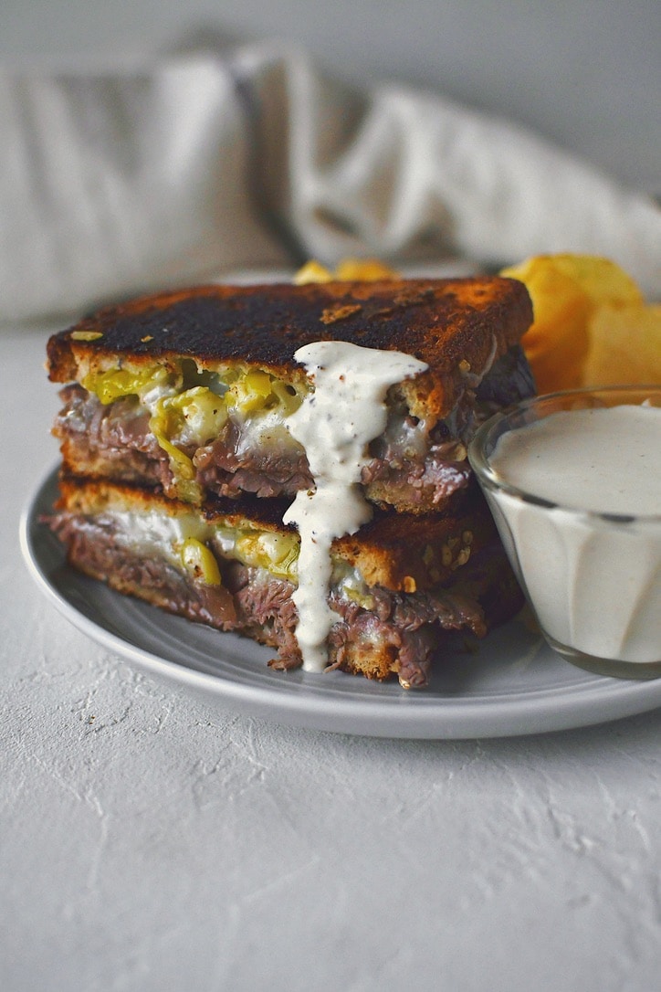 A roast beef grilled cheese sandwich that has been dipped in horseradish cream sauce.