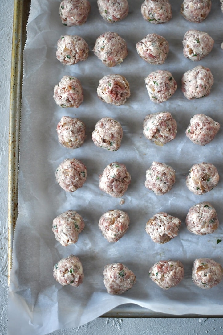 Portioned out meatball mixture into tiny meatballs, on a tray and rolled into uniform balls.
