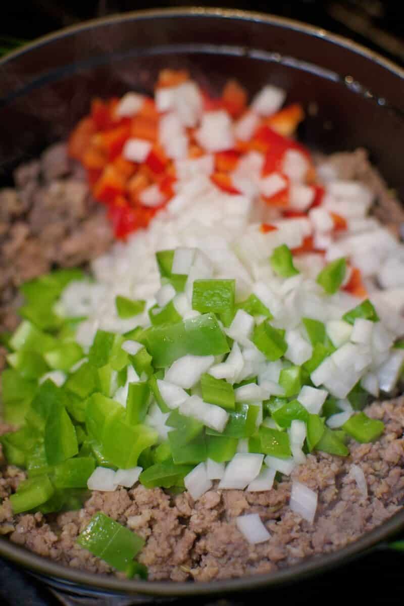 Adding the chopped vegetables to the pot of browned meat.