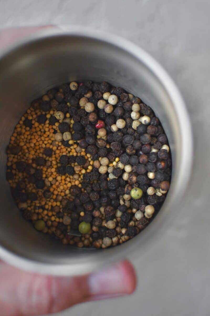 Placing the whole seeds and peppercorns in a spice grinder, before grinding.
