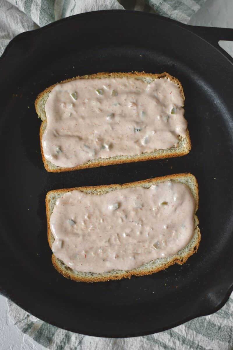Placing buttered bread in a hot pan, and spreading russian dressing on both sides.