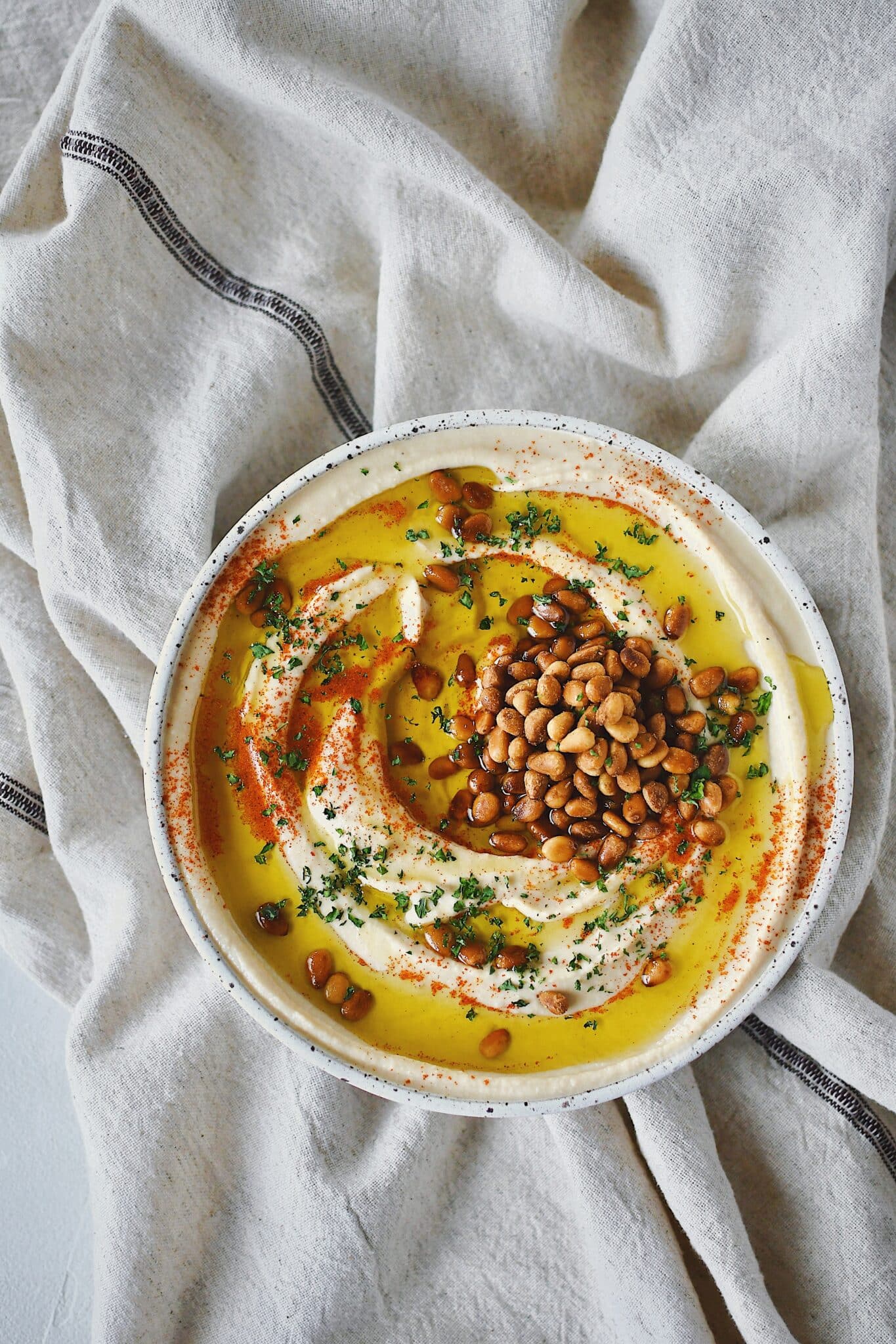 Homemade Hummus, topped with olive oil, paprika, toasted pine nuts, and parsley, ready to eat.