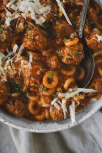 Homemade Spaghettios with meatballs in a bowl with a spoon topped with extra cheese and parsley.