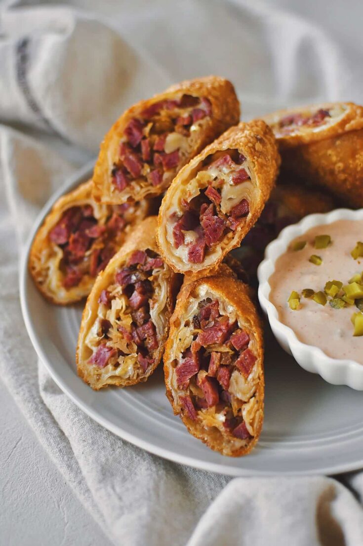Reuben Egg Rolls sliced in half on the diagonal and served on a plate with Russian Dressing.