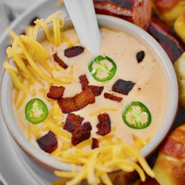 Beer Cheese Soup topped with more cheese, bacon bits, and serrano chili slices, ready to eat. Served with Kielbasa and Pretzel Bites