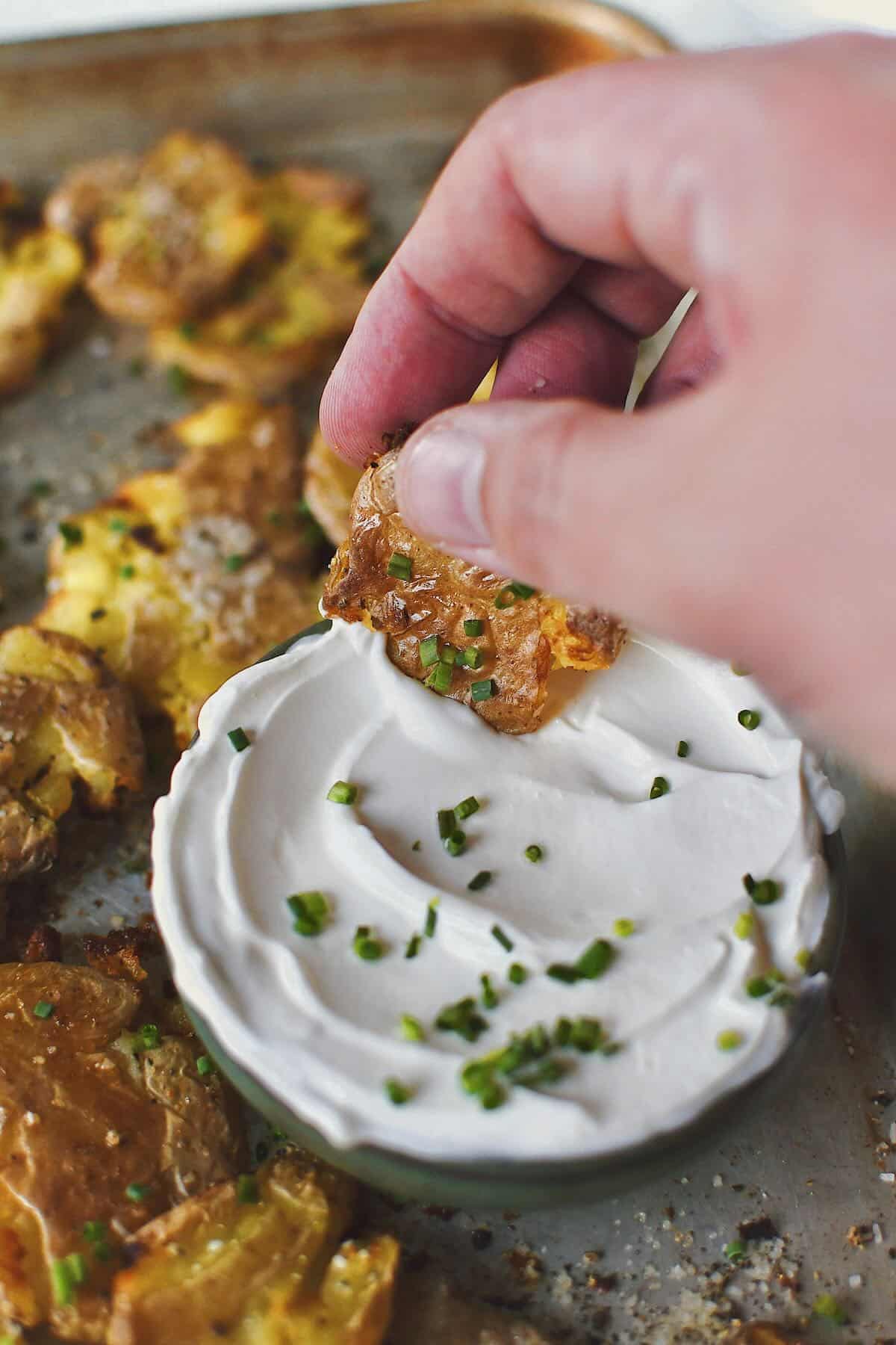 Crispy Smashed Potatoes with one being dipped in some chive sour cream.