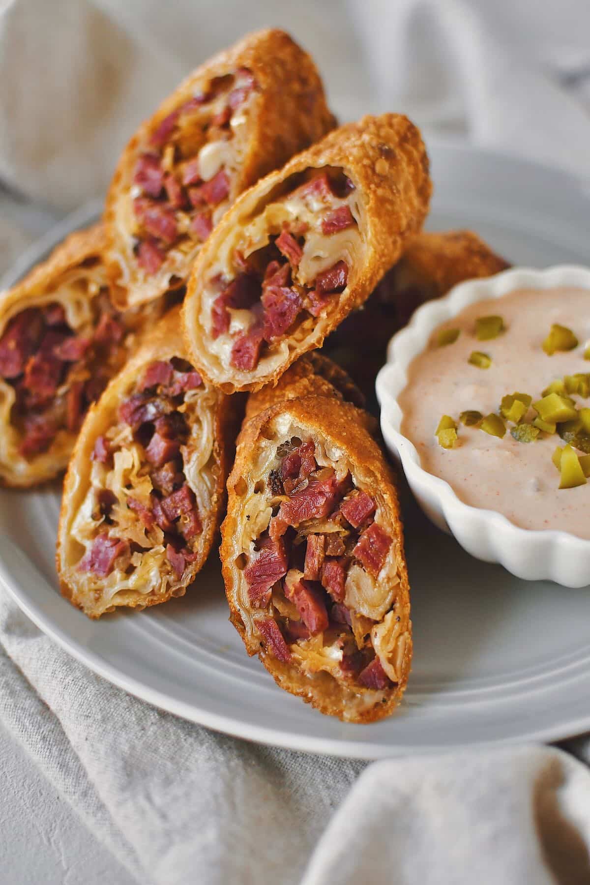 Reuben Egg Rolls sliced in half on the diagonal and served on a plate with Russian Dressing.