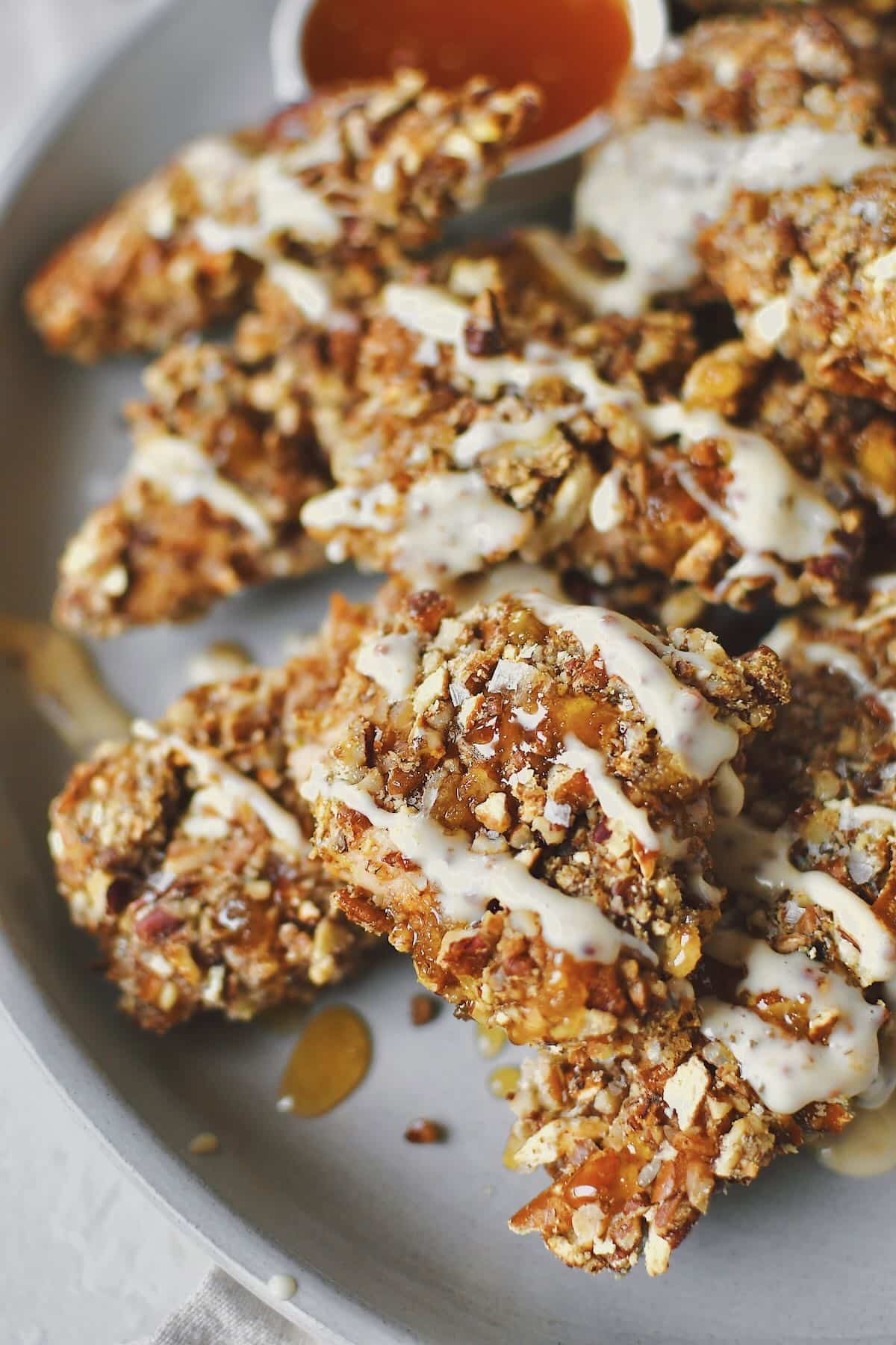 Pecan Crusted Chicken on a platter, served with honey and honey mustard dressing drizzled on top and on the side.