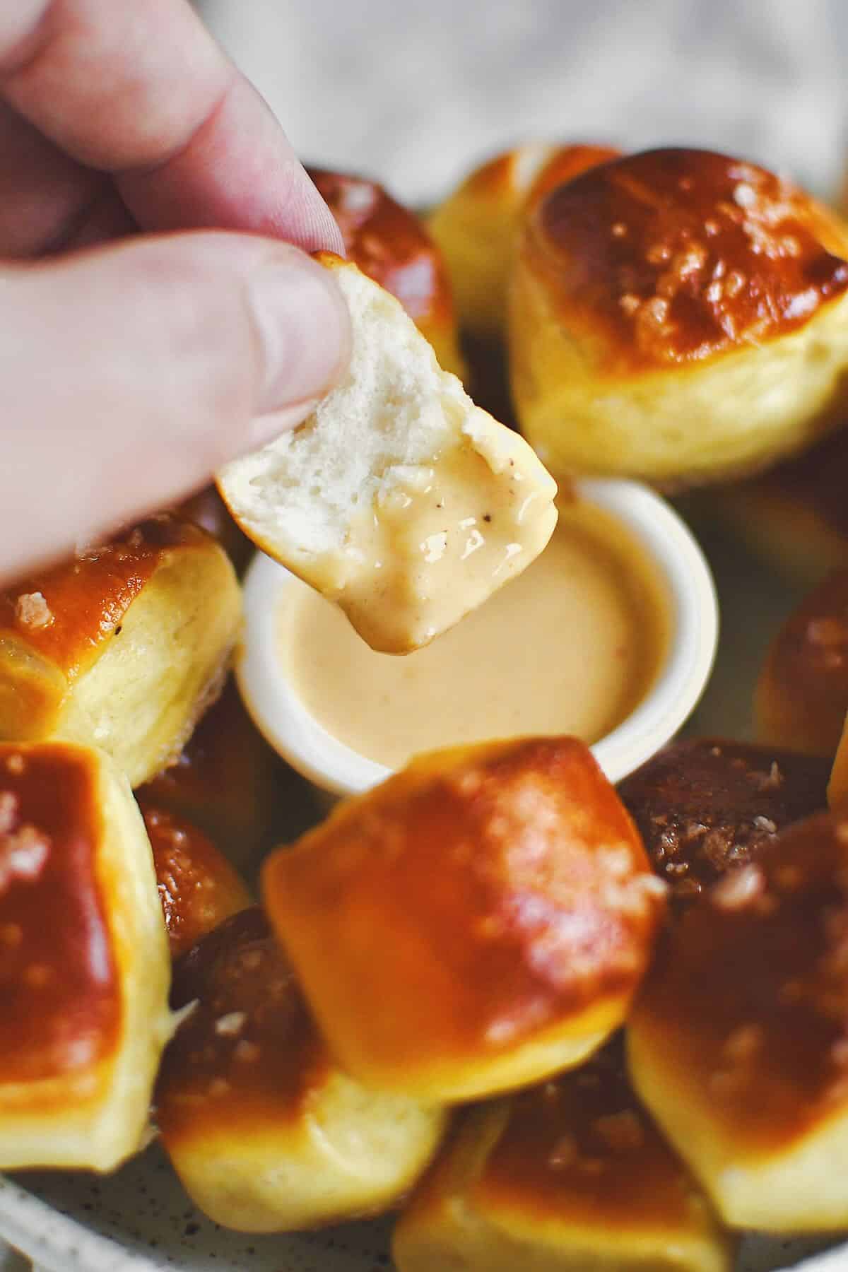 Dipping a split pretzel bite into cheese sauce before eating.