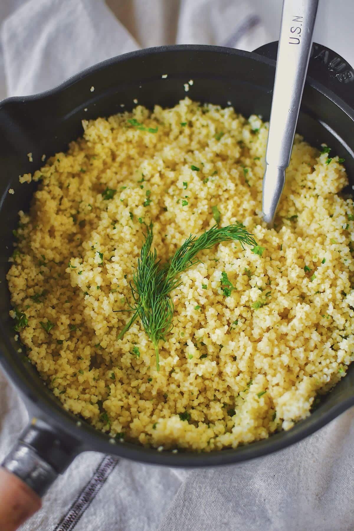 Finished couscous resting in the sauce pan, garnished with some fronds of dill.