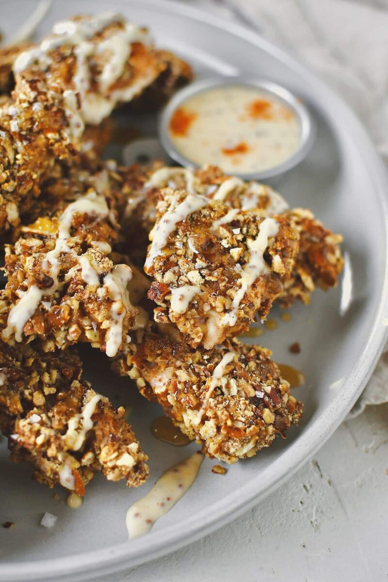 Pecan Crusted Chicken on a platter, served with honey and honey mustard dressing drizzled on top and on the side.