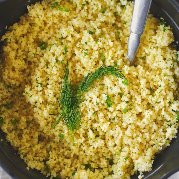 Finished couscous resting in the sauce pan, garnished with some fronds of dill.