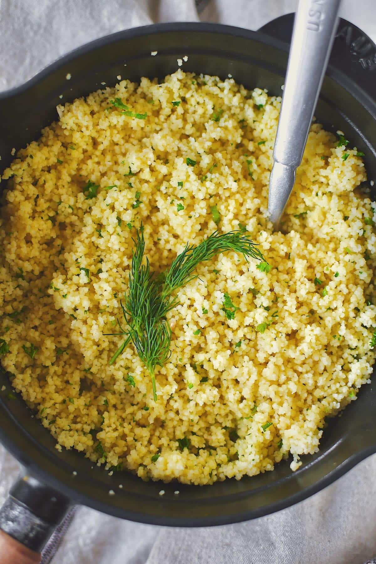 Finished couscous resting in the sauce pan, garnished with some fronds of dill.