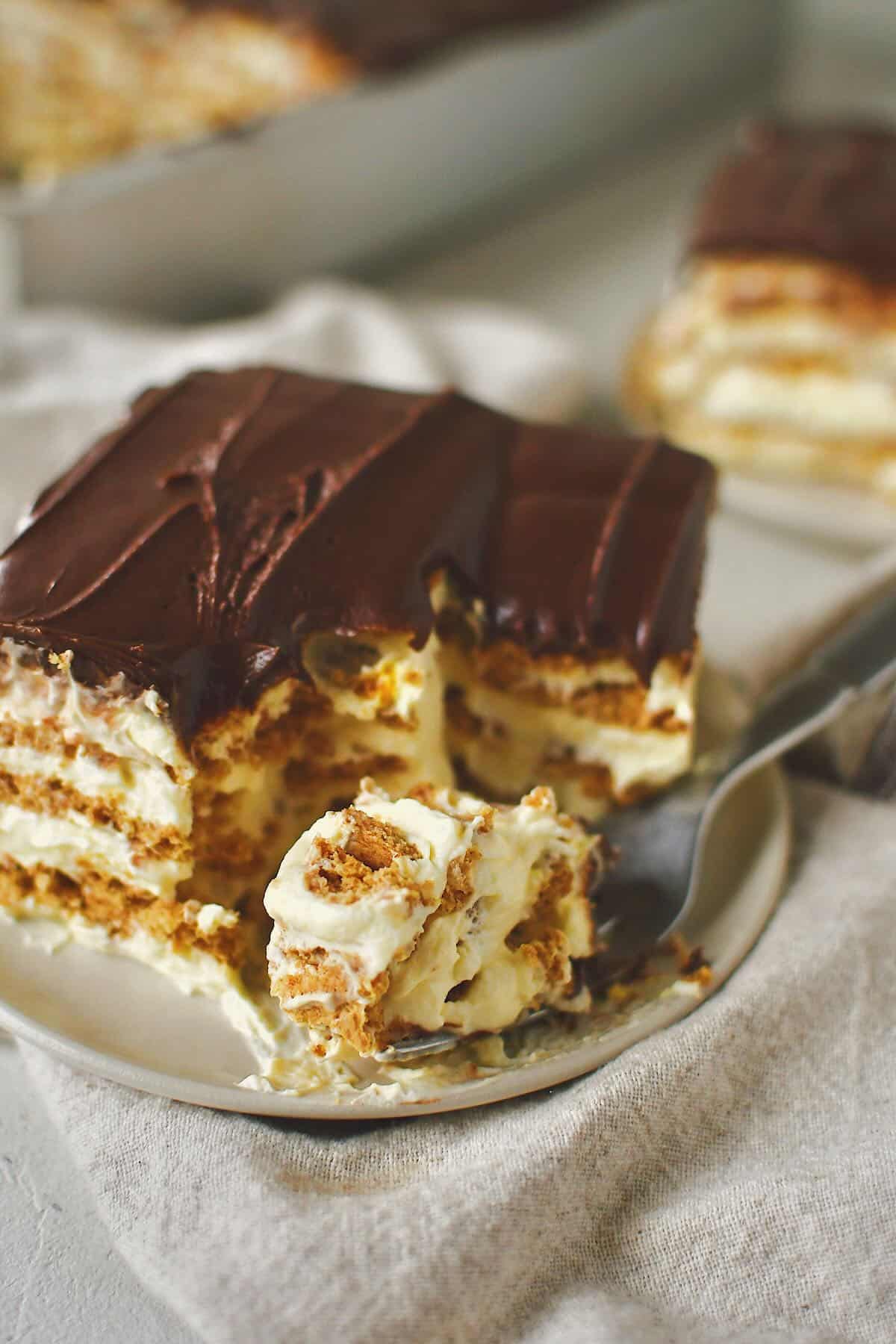Taking a bite out of a slice of eclair cake, some on a fork ready to be enjoyed.
