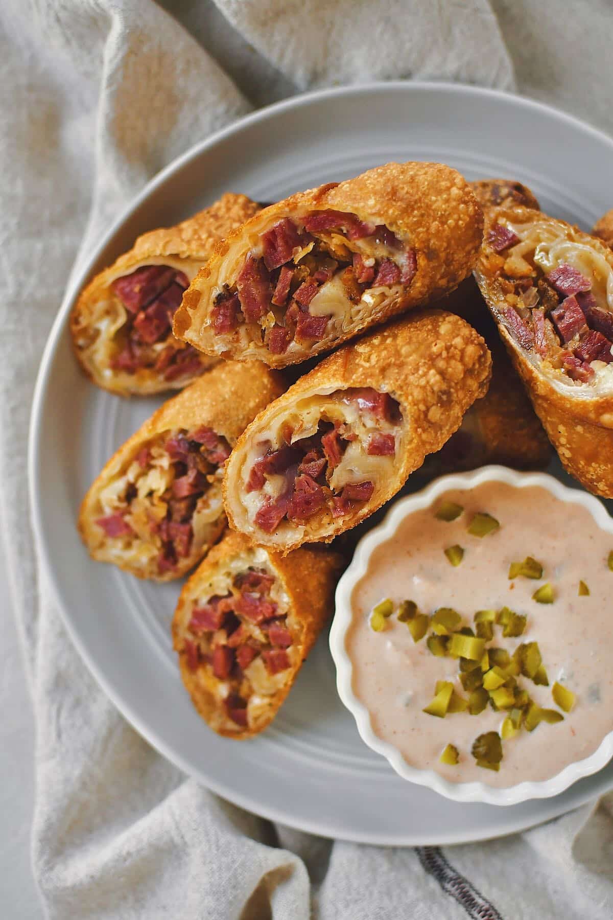 Reuben Egg Rolls sliced in half on the diagonal and served on a plate with Russian Dressing.