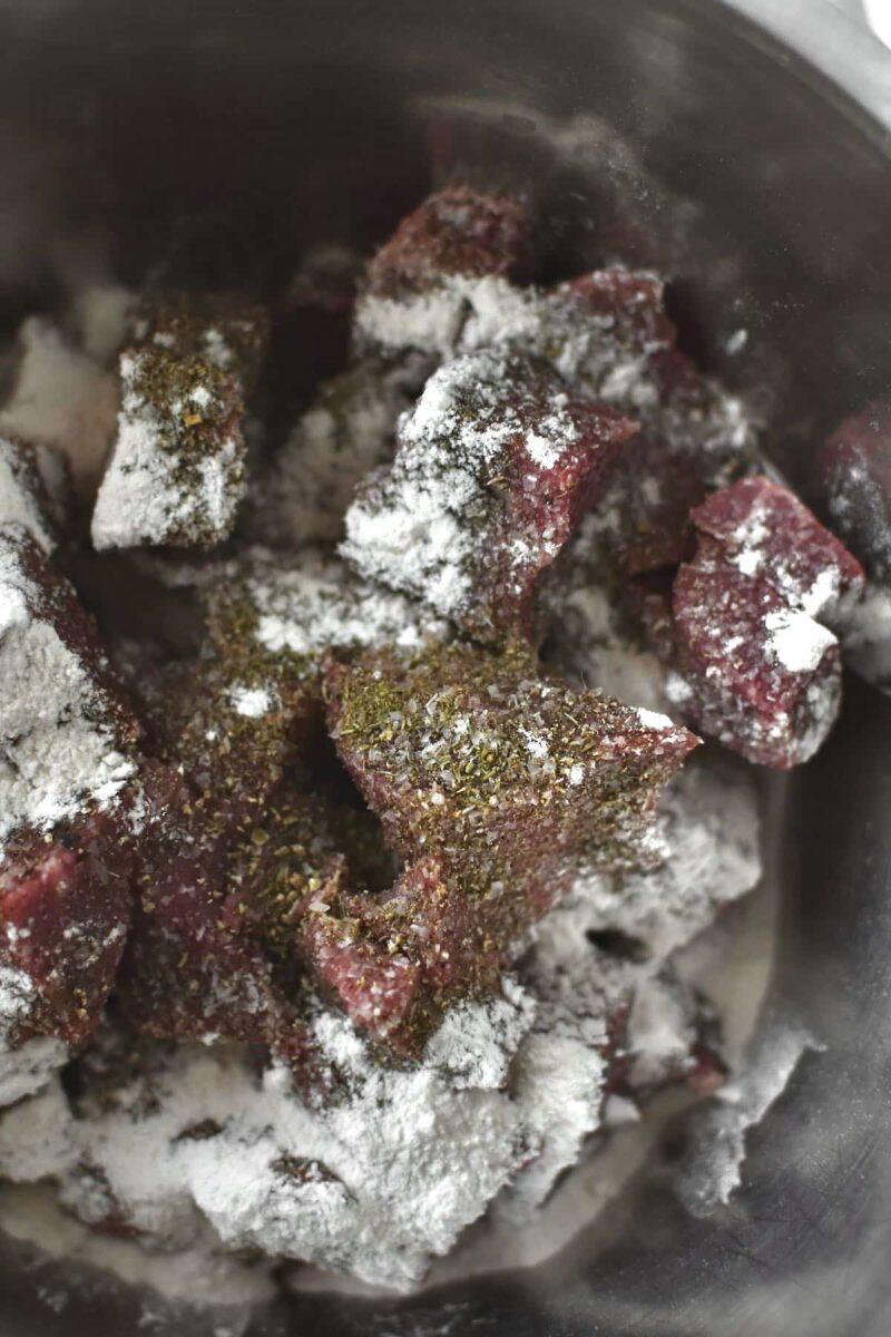 Seasoning the steak and dusting it with flour.