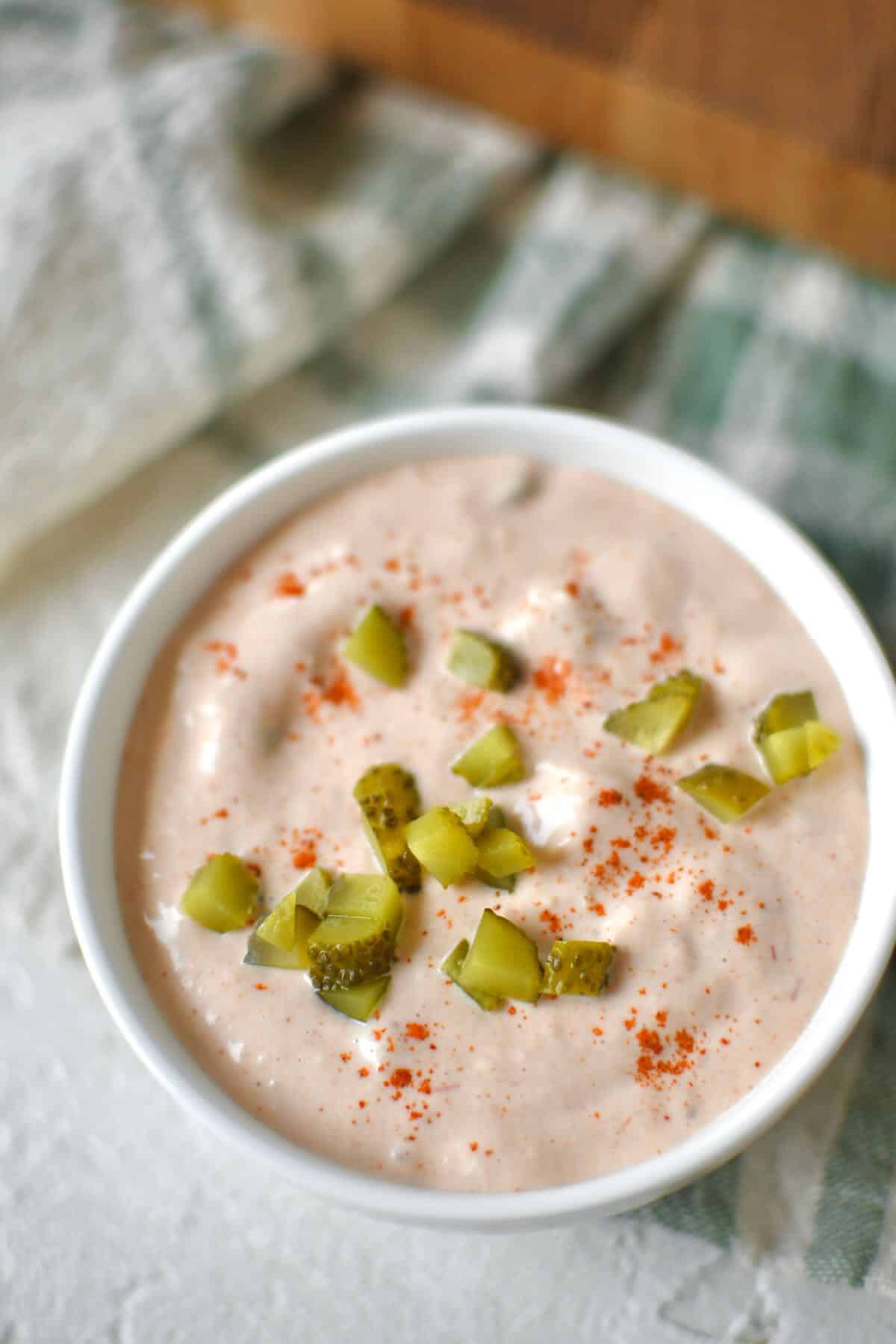 Complete Russian dressing recipe in a bowl topped with a sprinkle of paprika and chopped pickles.