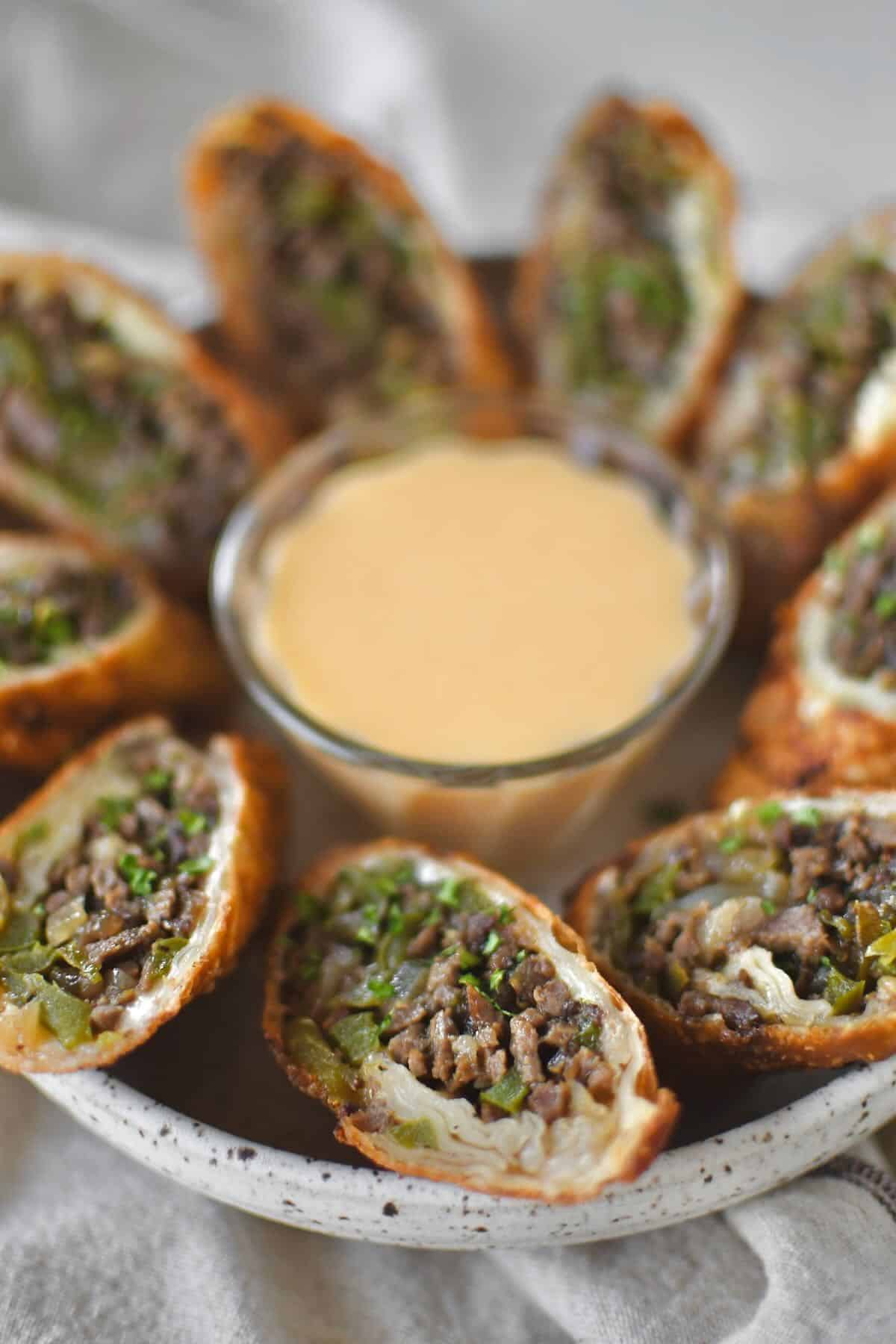 Philly Cheesesteak Egg Rolls cut in half and served with cheese sauce for dipping.