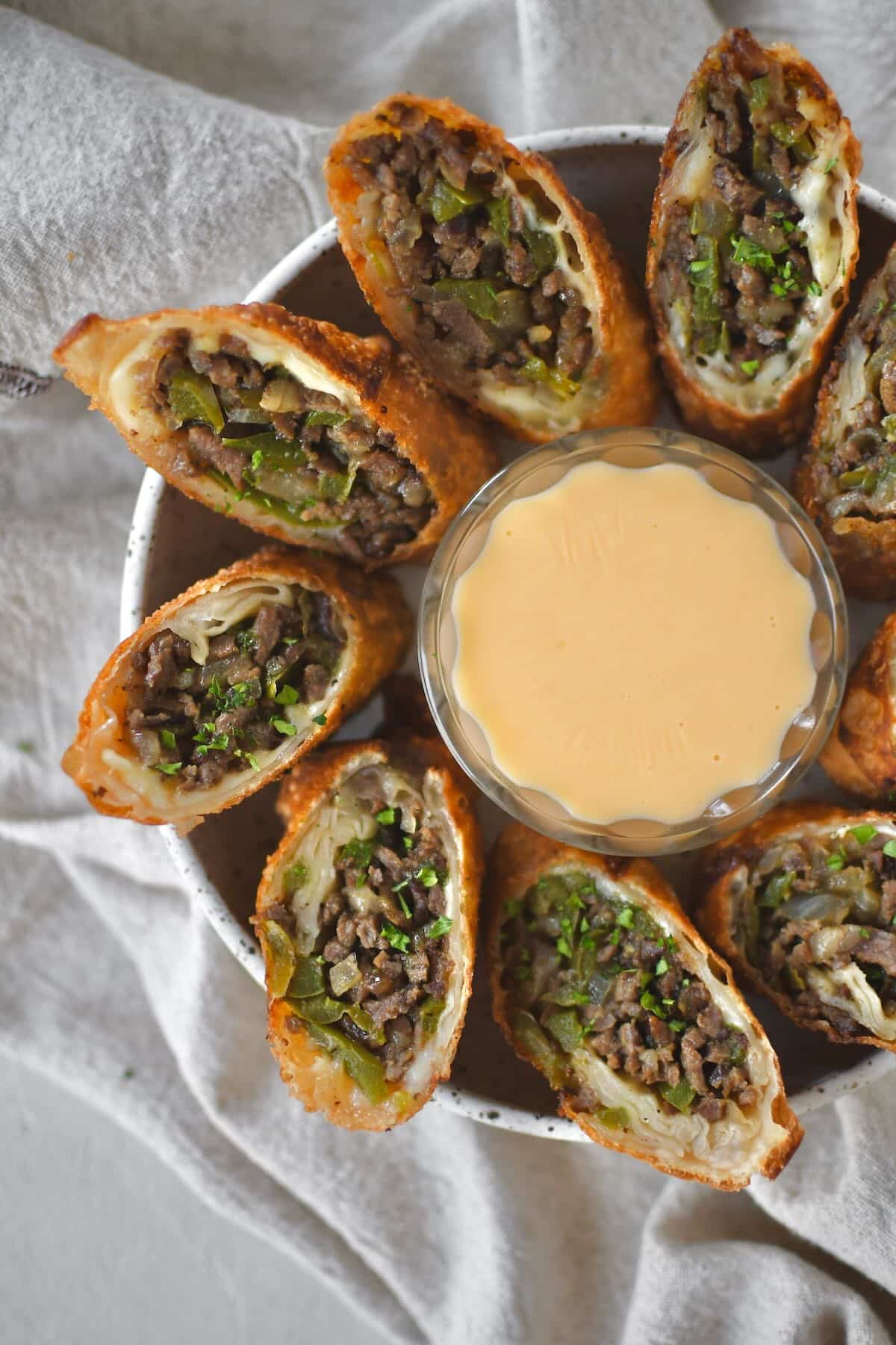 Philly Cheesesteak Egg Rolls cut in half and served with cheese sauce for dipping.