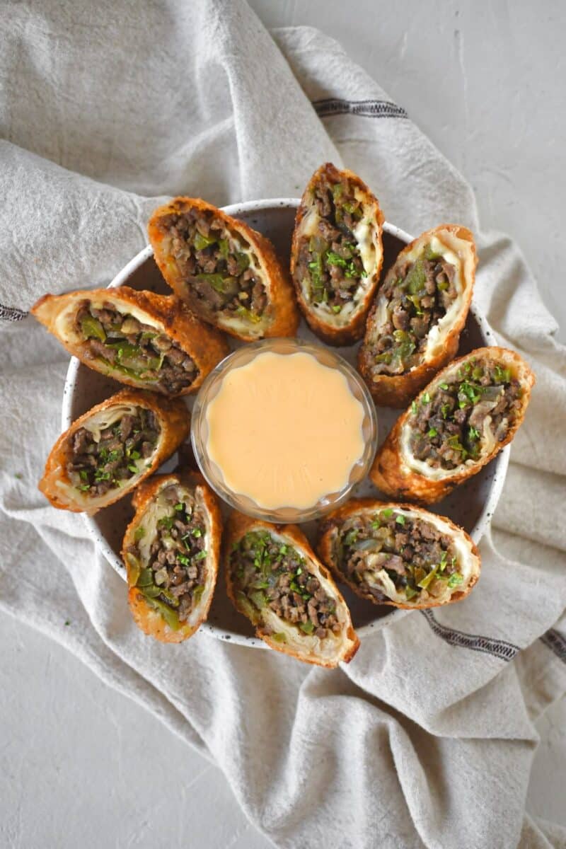 Philly Cheesesteak Egg Rolls cut in half and served with cheese sauce for dipping.