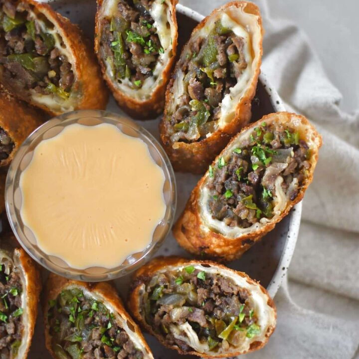 Philly Cheesesteak Egg Rolls cut in half and served with cheese sauce for dipping.