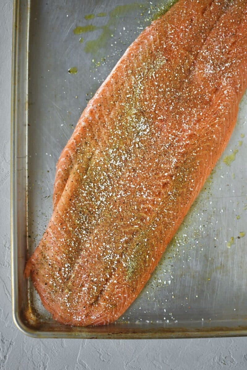 Seasoning the salmon side with Greek seasoning, salt, and pepper.