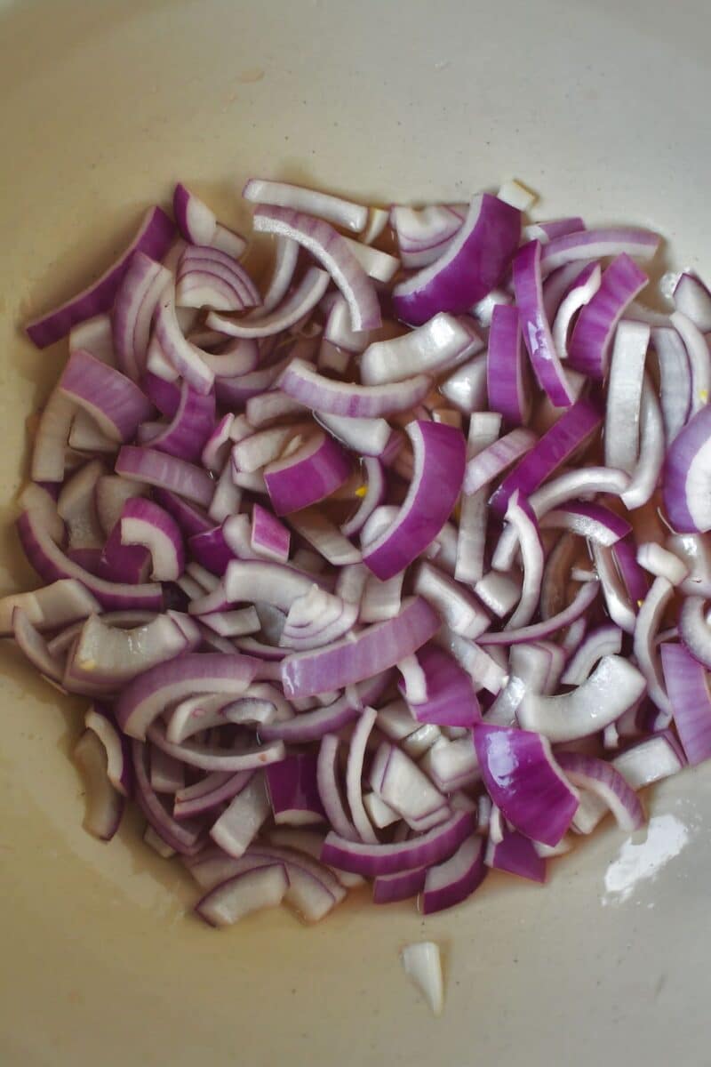 Sliced red onion in a large bowl with red wine vinegar before marinating.