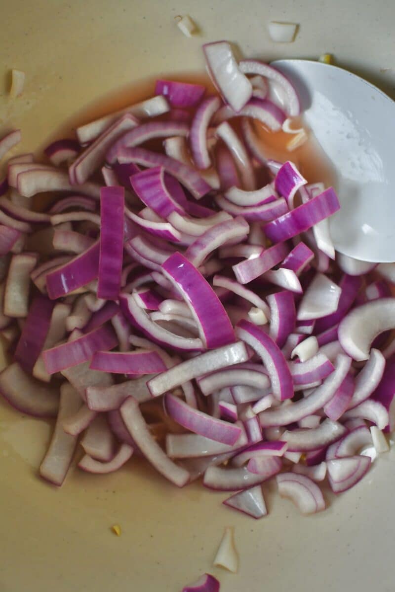 Sliced red onion in a large bowl with red wine vinegar after marinating.