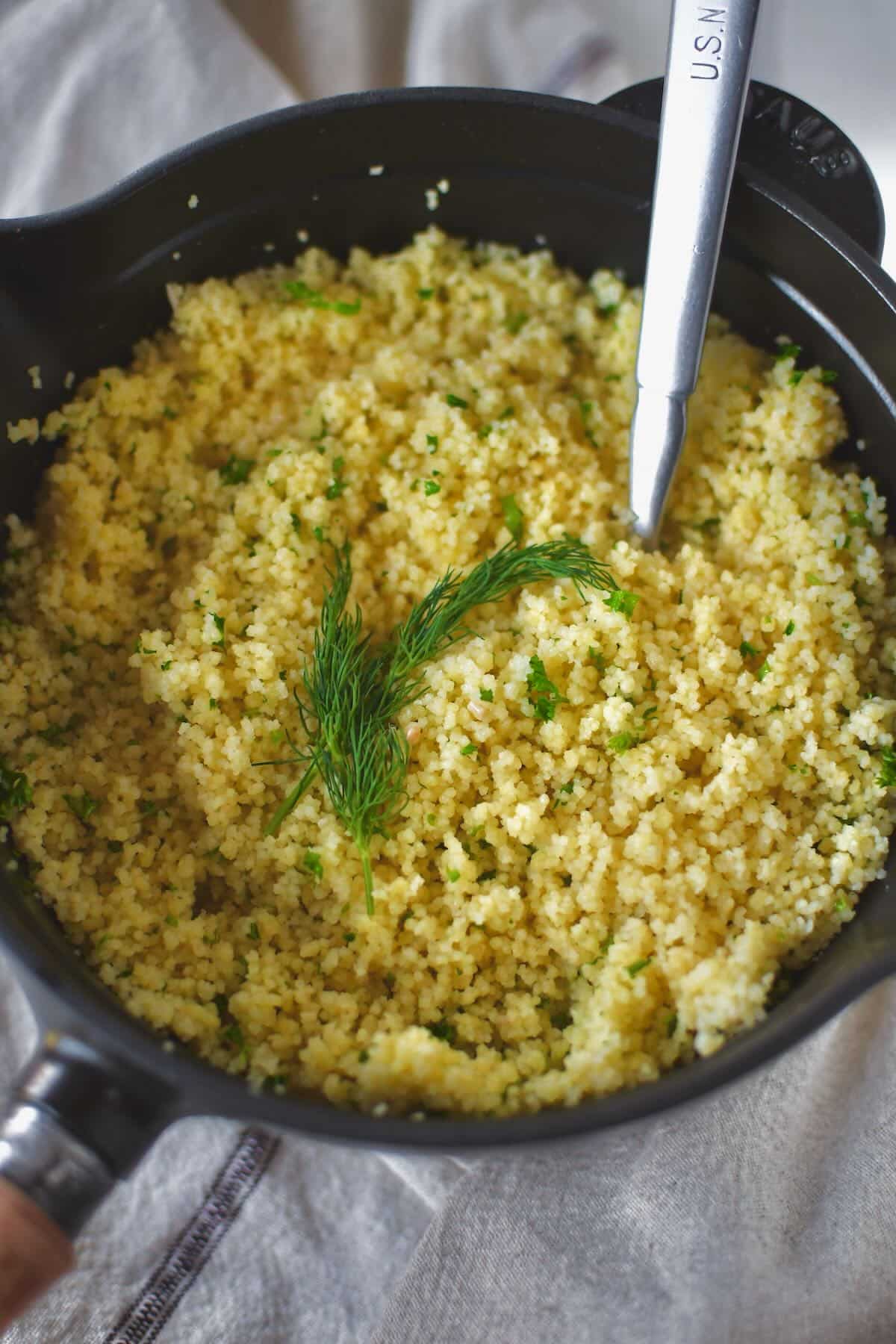 Finished couscous resting in the sauce pan, garnished with some fronds of dill.