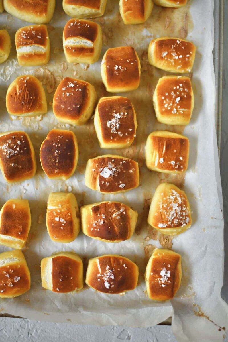 Pretzel bites lined up on a sheet pan and some of the dusted with flakey salt, after baking.