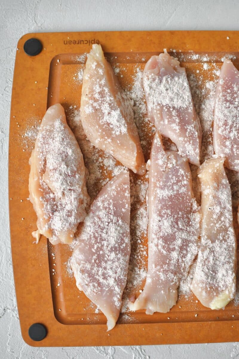 Seasoning tenderized chicken breasts that have been cut into strips for "chicken fingers".