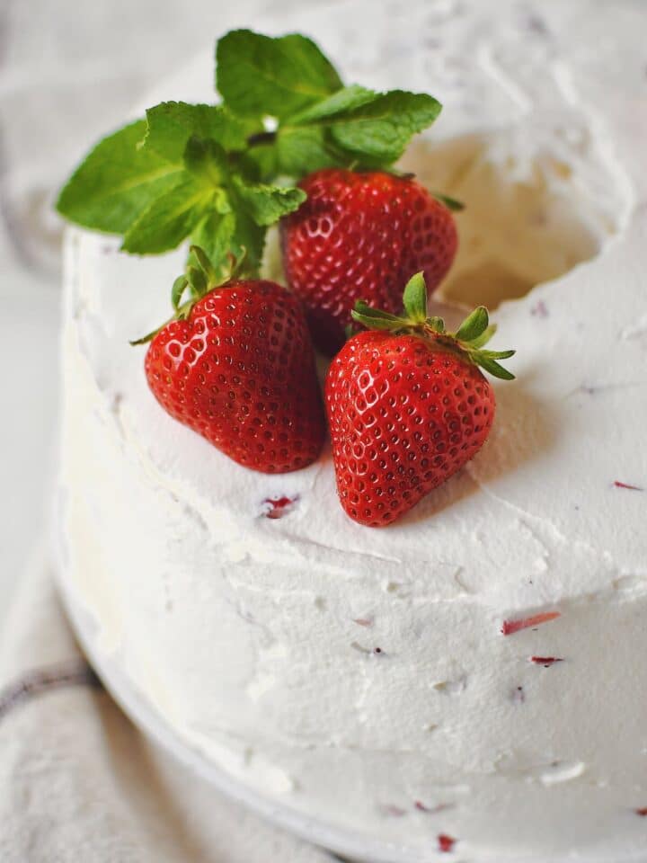 Strawberry Angel Food Cake just after frosting topped with whole strawberries and mint.