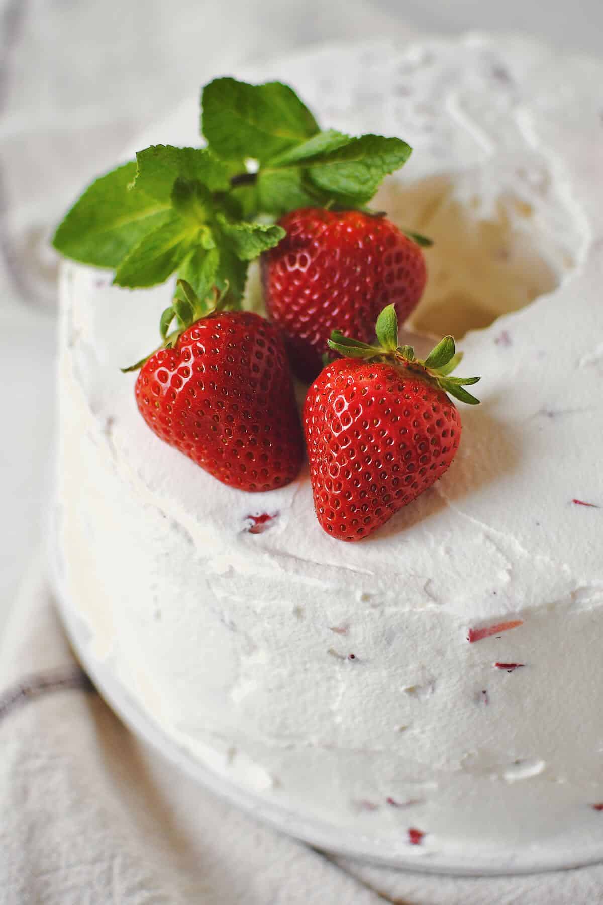 Strawberry Angel Food Cake just after frosting topped with whole strawberries and mint.
