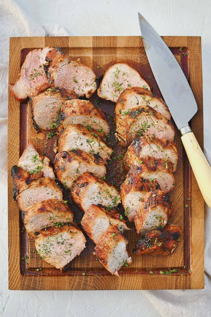 Grilled Pork Tenderloin sliced and resting on a cutting board with the knife on the side.