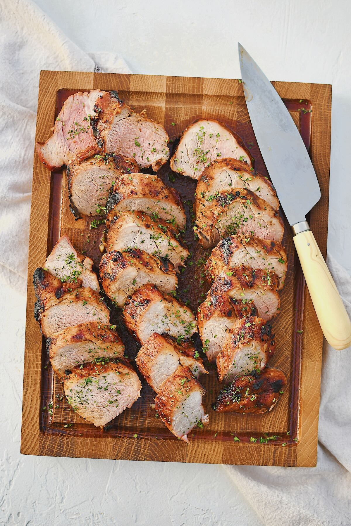 Grilled Pork Tenderloin sliced and resting on a cutting board with the knife on the side.