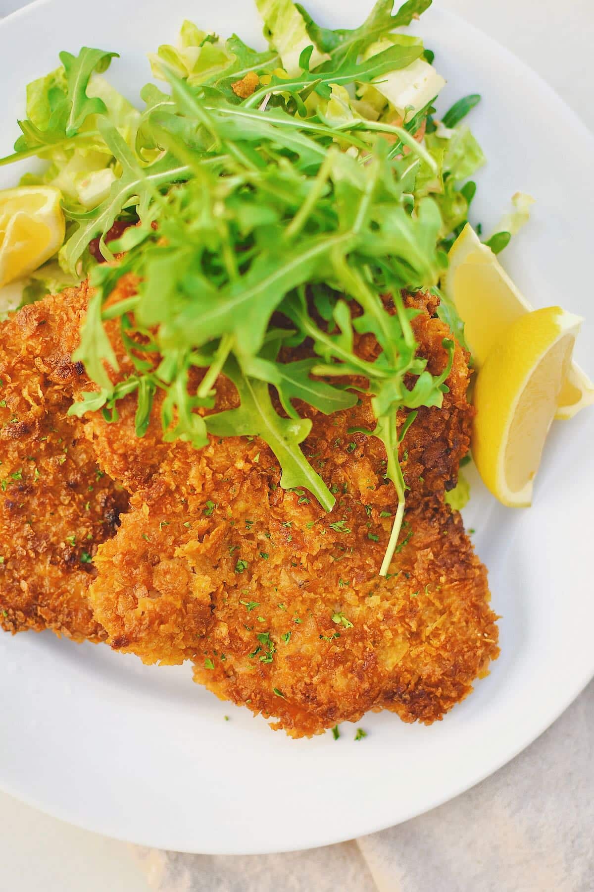 Pork Schnitzel on a plate, served with an arugula salad and lemon wedges.