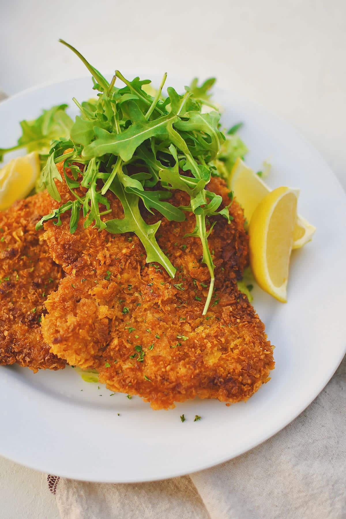 Pork Schnitzel on a plate, served with an arugula salad and lemon wedges.