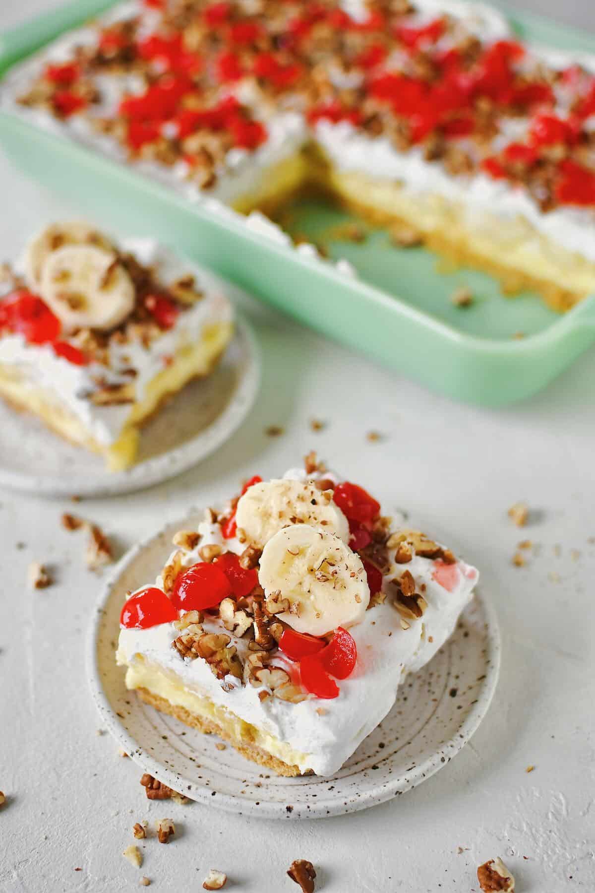 Banana Split Cake in the baking dish, a couple of slices removed and ready to eat that have been topped with banana slices just before serving.