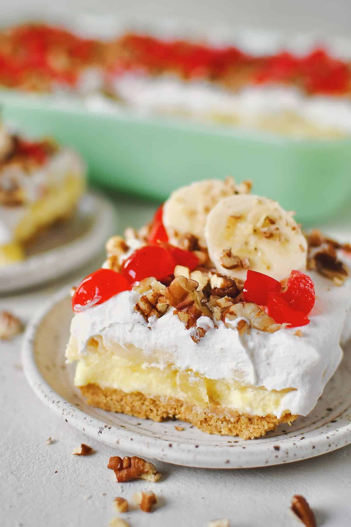 Banana Split Cake in the baking dish, a couple of slices removed and ready to eat that have been topped with banana slices just before serving.