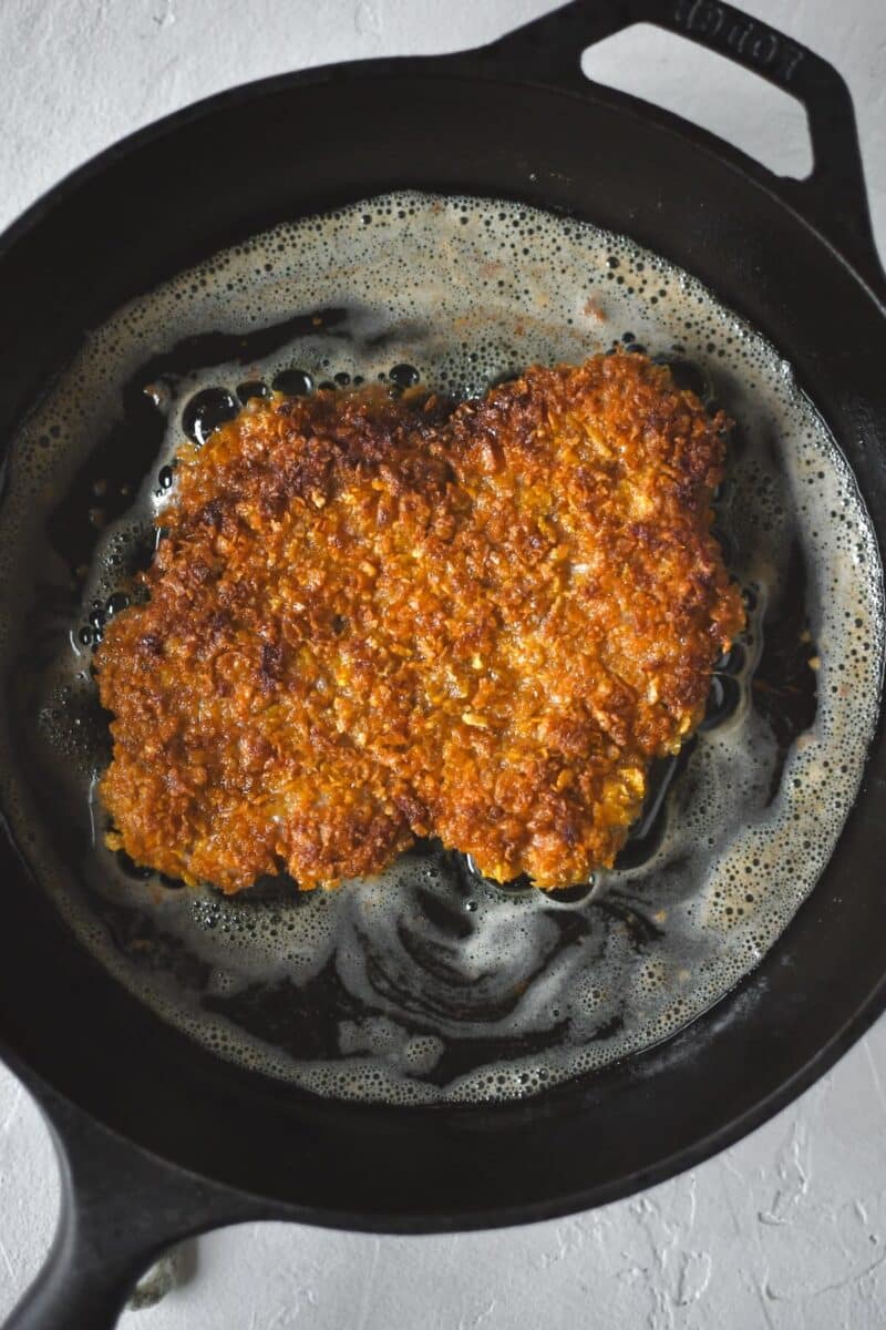 Pork cutlet that has been breaded, frying in a cast-iron skillet.