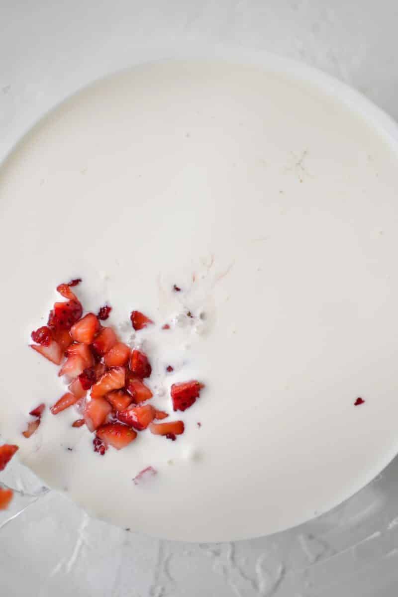Heavy cream and macerated strawberries in the bowl of a stand mixer, before whipping.
