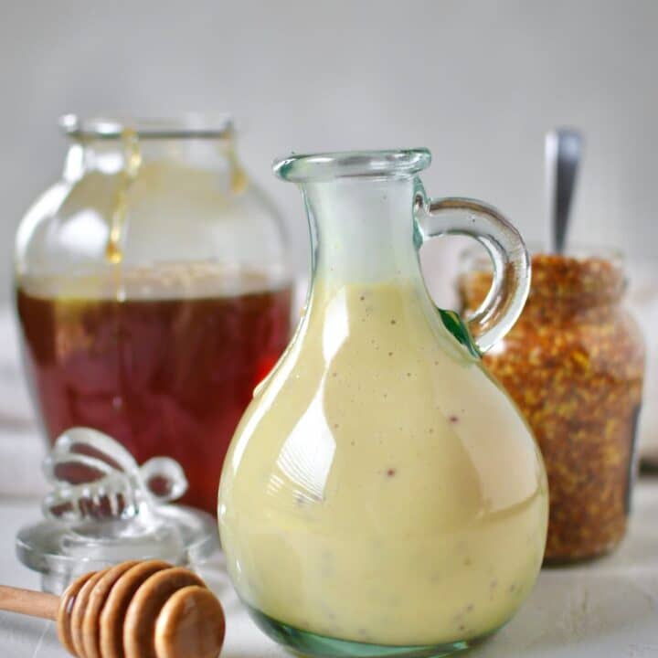 Dressing mixed up and placed in a storage bottle for later use. A honey jar and mustard jar sit behind it with a dripping honey dipper in front.
